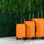 three orange suitcases sitting on a pedestal in front of a green wall